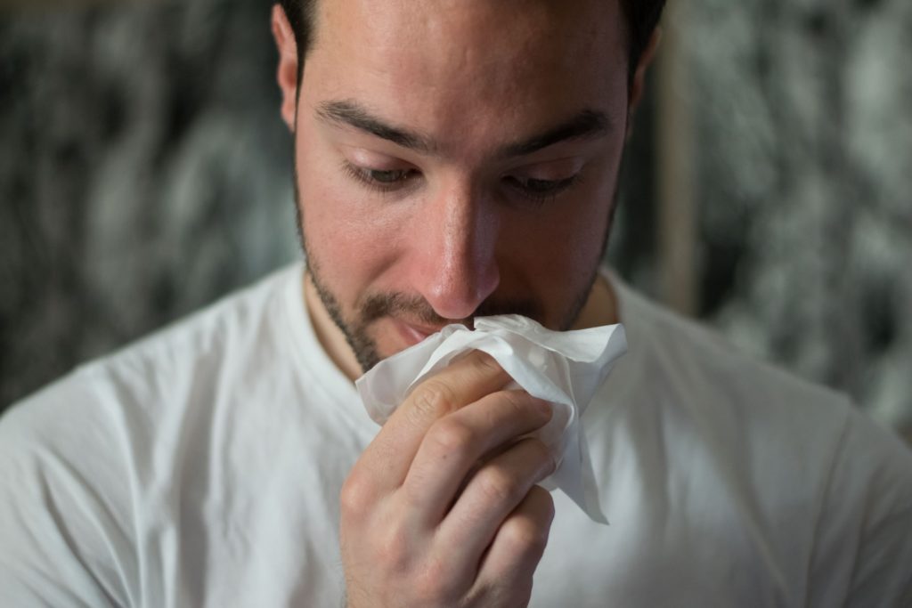 Mann mit Allergie Symptomen putzt sich die Nase mit einem Taschentuch