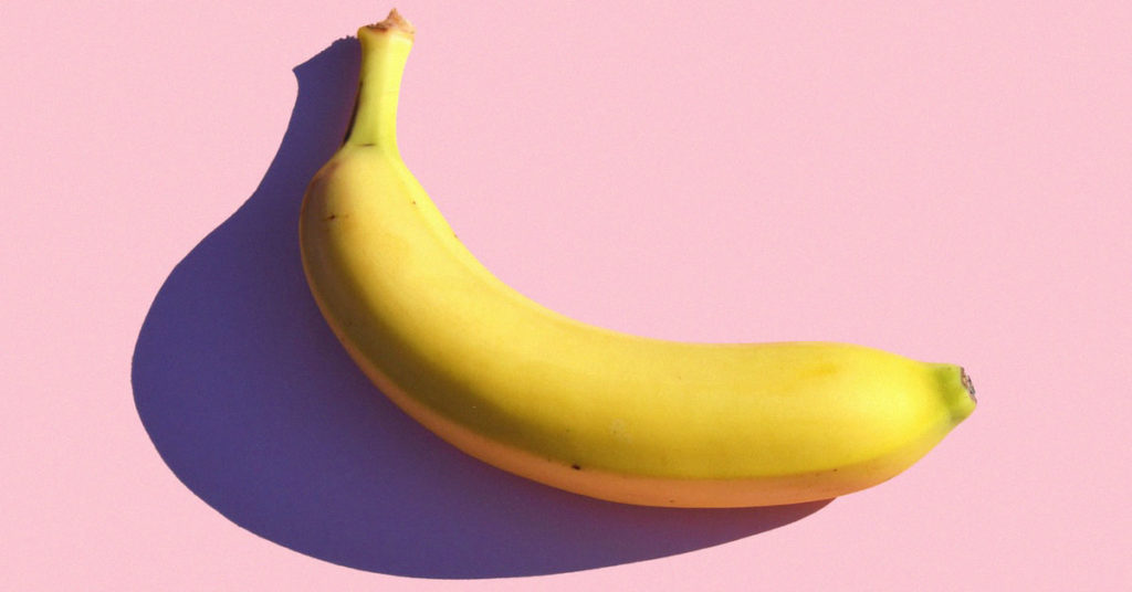 Eine schöne, gelbe Banane wirft einen Schatten auf einen rosa Hintergrund. Viele Menschen leiden an einer Bananenunverträglichkeit.
