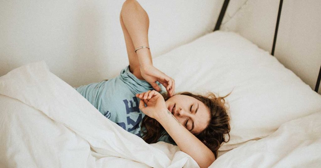 Foto von einer Frau, die im Bett liegt und müde ist. Müdigkeit ist ein Symptom von Ferritinmangel.