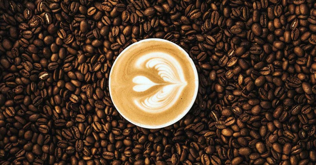 Eine Tasse Kaffee, umgeben von Kaffeebohnen. Viele Menschen haben eine Kaffee Unverträglichkeit. 