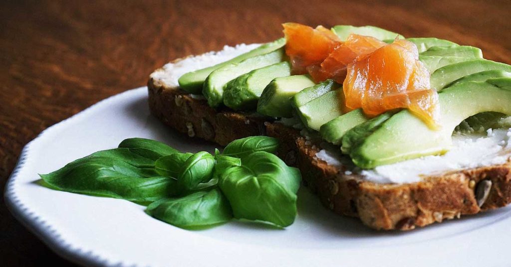 Auf diesem Foto sieht man ein Brot, das mit Avocado und Lachs belegt ist. Diese Lebensmittel können helfen, einen Omega 3 Mangel auszugleichen.