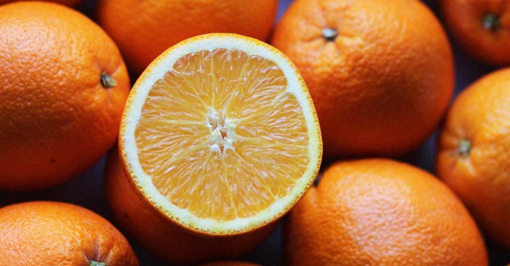 Einige ganze und eine aufgeschnittene Orange. Diese Orangen können eine Orangenallergie auslösen.